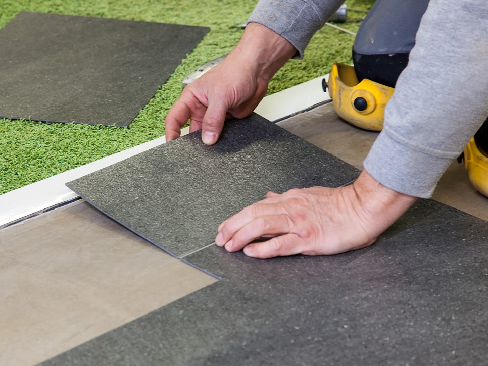 Verlegung von Bodenplatten durch einen Handwerker Nahaufnahme von Händen beim Einpassen und Verkleben grauer Bodenplatten während der Verlegearbeit